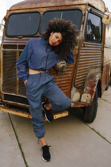 Portrait of stylish young woman wearing tracksuit leaning against old van - AGGF00018