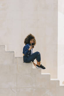 Stylish young woman wearing tracksuit and using cell phone on stairs - AGGF00020