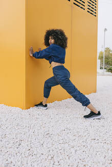 Stylish young woman doing stretching exercise at a yellow wall - AGGF00038