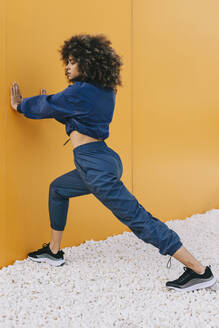 Stylish young woman doing stretching exercise at a yellow wall - AGGF00040