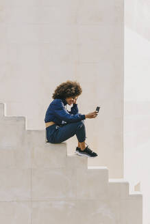 Stylische junge Frau im Trainingsanzug und mit Handy auf einer Treppe im Freien - AGGF00043