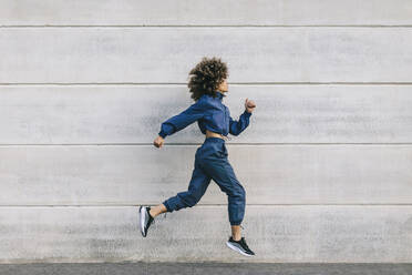 Stylish young woman running along concrete wall - AGGF00054