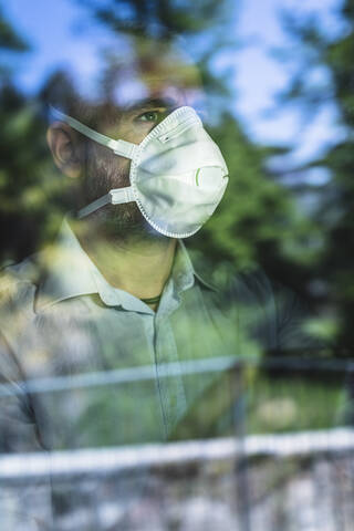 Mature pensive man with protective mask looking out of the window stock photo
