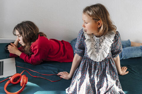 Zwei Schwestern mit Kopfhörern und Laptop auf dem Bett liegend, lizenzfreies Stockfoto