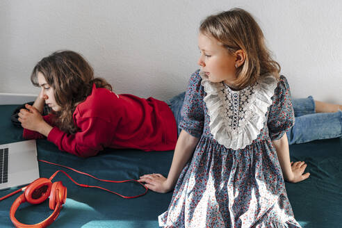 Zwei Schwestern mit Kopfhörern und Laptop auf dem Bett liegend - OGF00267