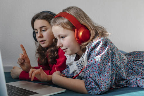 Zwei Schwestern mit Kopfhörern liegen zusammen auf dem Bett und schauen auf einen Laptop - OGF00269