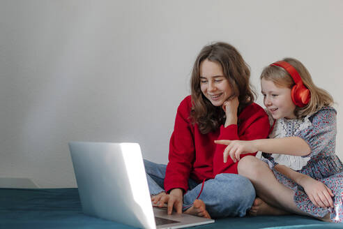 Porträt von zwei Schwestern, die zusammen auf einem Bett sitzen und auf einen Laptop schauen - OGF00273