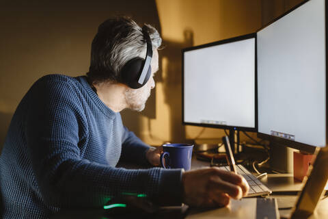 Älterer Mann sitzt am Schreibtisch zu Hause und arbeitet mit Grafiktablett und Computer, lizenzfreies Stockfoto