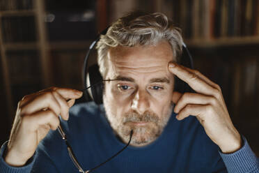 Portrait of pensive mature man with headphones in front of computer - MCVF00299