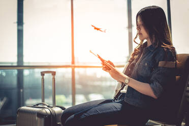 Woman Using Smart Phone While Sitting At Departure Area In Airport - EYF04014