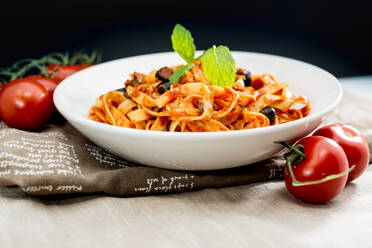 Nahaufnahme von Nudeln mit Tomaten auf dem Tisch vor schwarzem Hintergrund - EYF04158