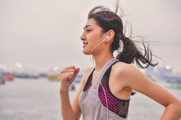 Woman Listening Music While Jogging By River Against Sky - EYF04171