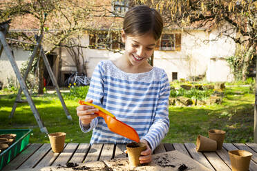 Girl filling nursery pots with soil and seeds - LVF08789