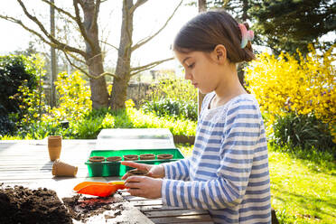 Girl filling nursery pots with soil and seeds - LVF08790