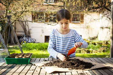 Girl filling nursery pots with soil and seeds - LVF08793