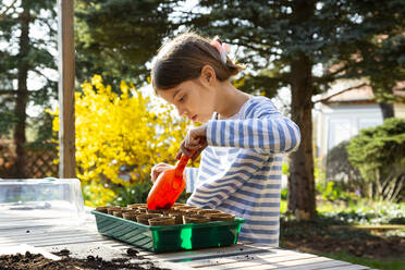 Girl filling nursery pots with soil for her little greenhouse - LVF08796