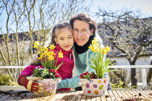 Porträt einer glücklichen Mutter und ihrer Tochter, die gemeinsam auf dem Balkon Blumen pflanzen - DIKF00447