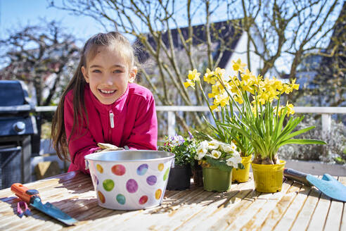 porträt eines glücklichen Mädchens, das auf dem Balkon Blumen pflanzt - DIKF00449