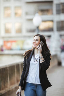 Porträt einer glücklichen Frau am Telefon beim Spaziergang in der Stadt - LJF01504