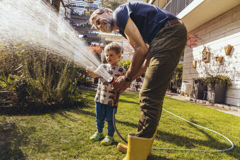 Vater und Sohn wässern den Rasen im Garten, lizenzfreies Stockfoto