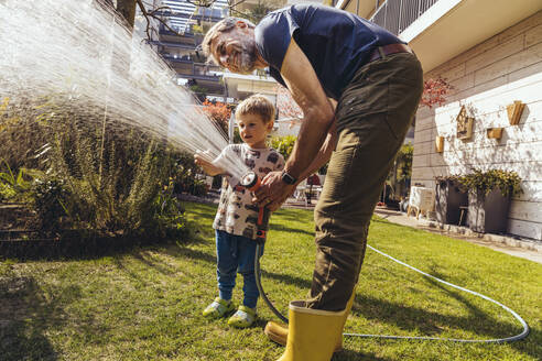 Father and son watering the lawn in garden - MFF05569