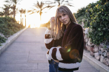 Young woman wearing fur jacket standing on street during sunset - MPPF00765