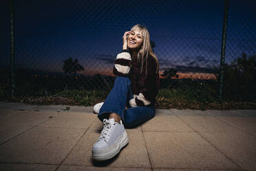 Young woman wearing fur jacket, sitting on the ground at night - MPPF00769