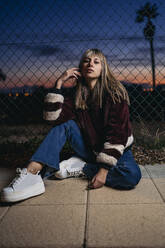 Young woman wearing fur jacket, sitting on the ground at night - MPPF00773