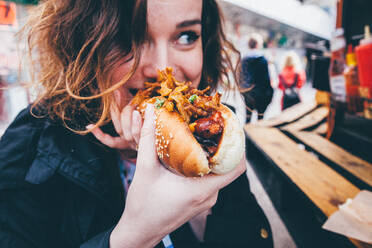 Nahaufnahme einer jungen Frau, die einen Hot Dog auf der Straße isst - EYF04210