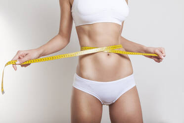 Midsection Of Young Woman Measuring Abdomen Against White Background - EYF04225