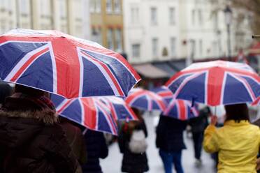 Rückansicht von Menschen zu Fuß auf der Straße mit Regenschirm - EYF04259