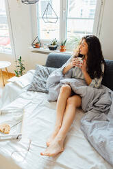 High Angle View Of Thoughtful Young Woman Looking Away While Having Coffee On Bed At Home - EYF04268