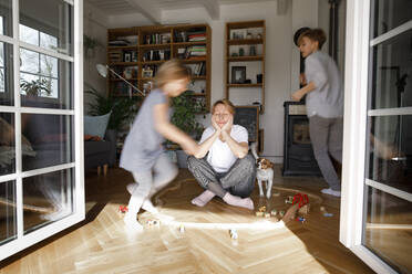 Gestresste Mutter, die in der Mitte des Spielzeugs sitzt, während die Kinder um sie herumlaufen - KMKF01288