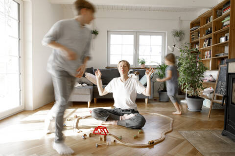 Mother meditating in the middle of toys, whilchirdren are running around her stock photo