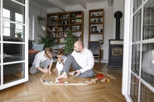 Vater und seine Kinder sitzen auf dem Boden und spielen mit einer Spielzeugeisenbahn - KMKF01302