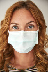 Portrait of red-haired woman wearing a protective mask at home - JHAF00073