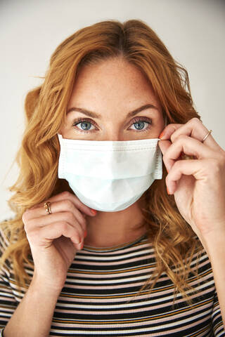 Portrait of red-haired woman wearing a protective mask at home stock photo