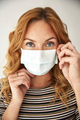 Portrait of red-haired woman wearing a protective mask at home - JHAF00074