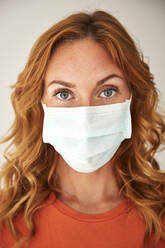 Portrait of red-haired woman wearing a protective mask at home - JHAF00075