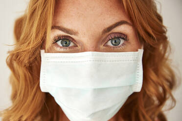 Portrait of red-haired woman wearing a protective mask at home - JHAF00077
