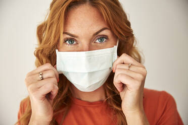 Portrait of red-haired woman wearing a protective mask at home - JHAF00078