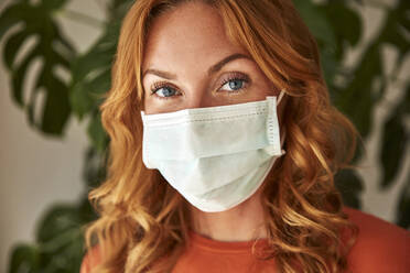 Portrait of red-haired woman wearing a protective mask at home - JHAF00079