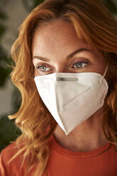 Portrait of red-haired woman wearing a protective mask at home - JHAF00081