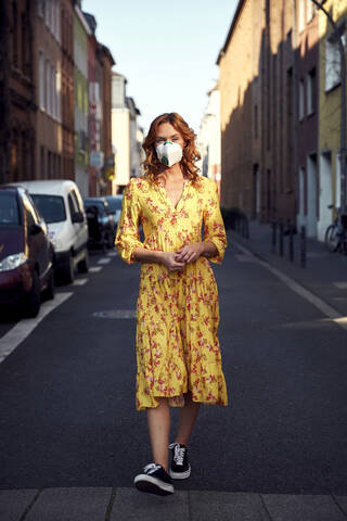 Red-haired woman wearing a FFP2 face mask and walking on empty road stock photo