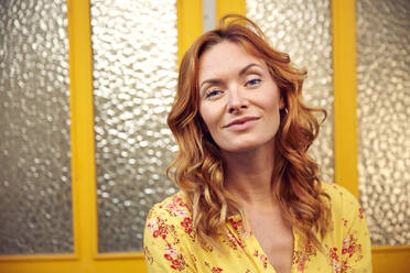 Portrait of red-haired happy woman in front of door, smiling at camera - JHAF00095