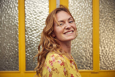 Portrait of red-haired happy woman in front of door, smiling at camera - JHAF00096