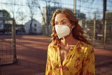 Portrait of red-haired woman wearing a FFP2 face mask in the city - JHAF00098