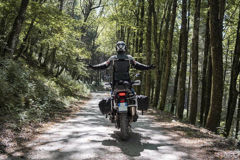 Motorradfahrer auf einem Waldweg mit ausgestreckten Armen - FBAF01507