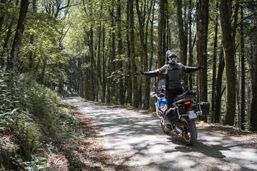 Motorradfahrer auf einem Waldweg mit ausgestreckten Armen - FBAF01508