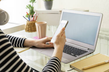 Nahaufnahme einer jungen Frau, die einen Laptop und ein Smartphone am Schreibtisch zu Hause benutzt - AFVF05967